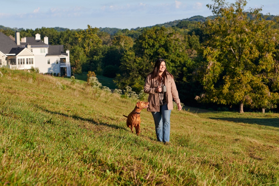 woman walking with coffee in field with vizsla pointer